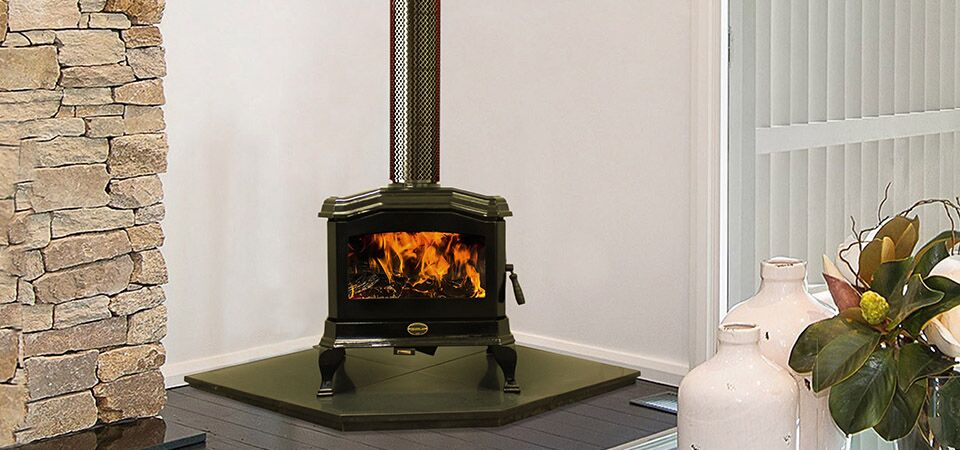 A black Kemlan C24 wood burning stove situated in a living room beside a white vase and a plant, one of the best wood heaters for autumn home heating