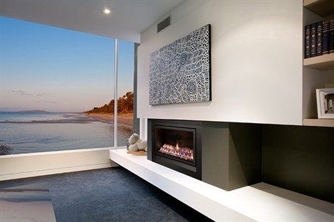 A modern living room with a Heatmaster Enviro Pebbles fireplace and ocean view, the best gas fireplaces for autumn warmth