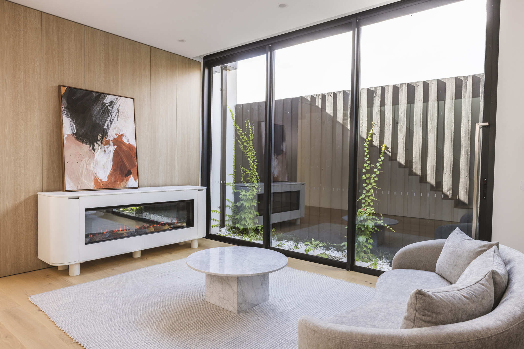 Modern living room with Ember Arc Grange 180 electric fireplace, a painting above, and large windows enhancing the open, stylish space