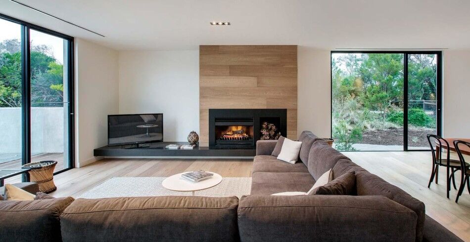 An open wood fireplace beside a cosy living room with a plush sofa and glass doors, one of the best wood heaters for autumn
