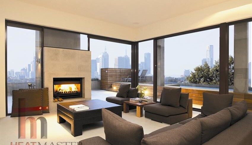 An open wood fireplace in a stylish living room with large windows that gives a nice city view, perfect for cosy warmth with the best wood heaters for autumn