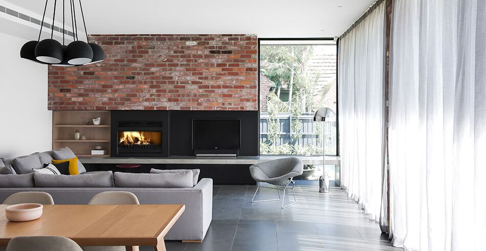 A black Open Wood fireplace with a glowing fire with an elegant sofa in a spacious living room, one of the best wood heaters for autumn to create a warm and cosy home atmosphere