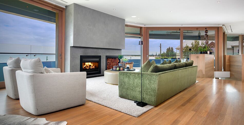 A cosy living room with a green couch, large glass windows and open wood fireplace, creating warmth and comfort with the best wood heaters for autumn