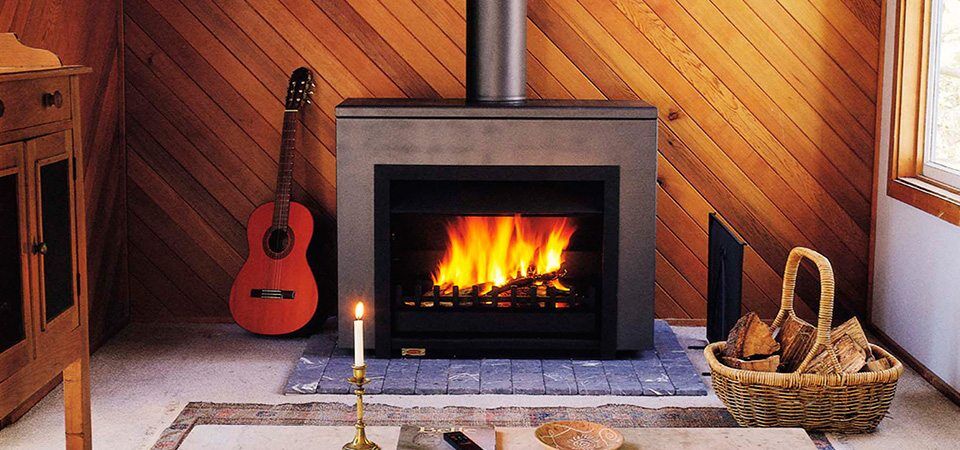 A Jetmaster Universal Freestanding wood burning stove beside a guitar in a cosy room setting