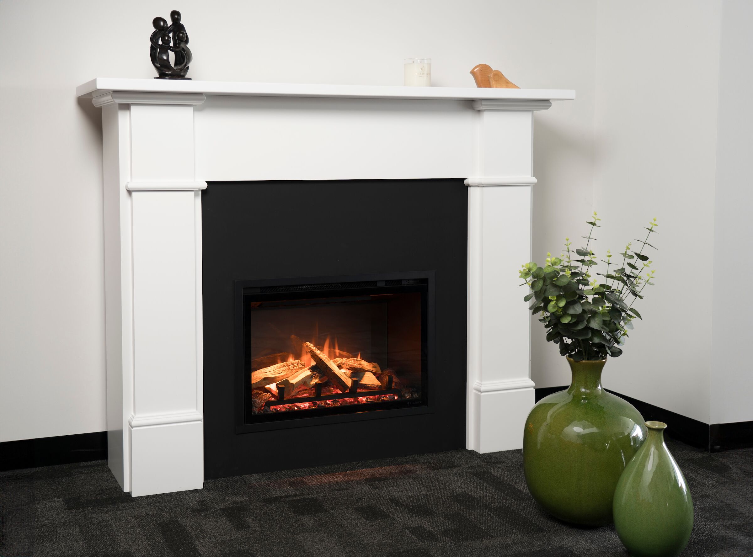Regency Ei25 Electric Fireplace Insert in a white case with a decorative vase on top, adding warmth and style to a cosy interior space