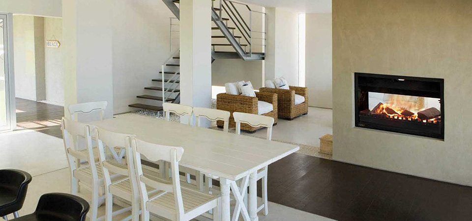 Jetmaster Universal Double Sided fireplace set in a white wall beside staircase and dining area, one of the best fireplaces for autumn warmth