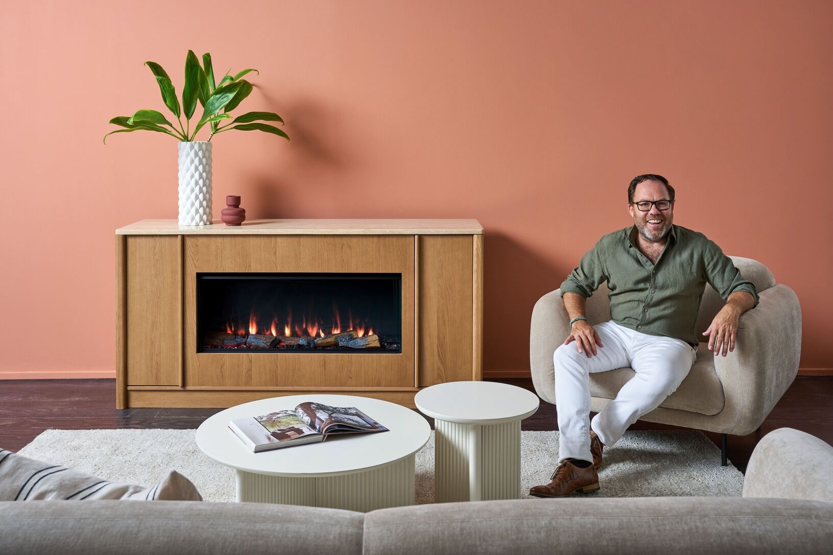 A man sits beside the Ember Arc Grange 180 electric fireplace in a cosy living room, adding warmth and comfort to the space