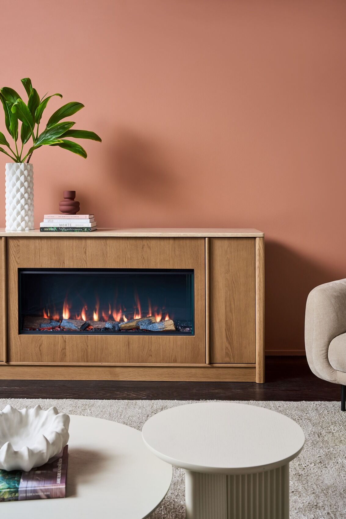 White vase and books on a wooden cabinet above the Ember Arc Grange 180 electric fireplace in a cosy, elegant living room setting