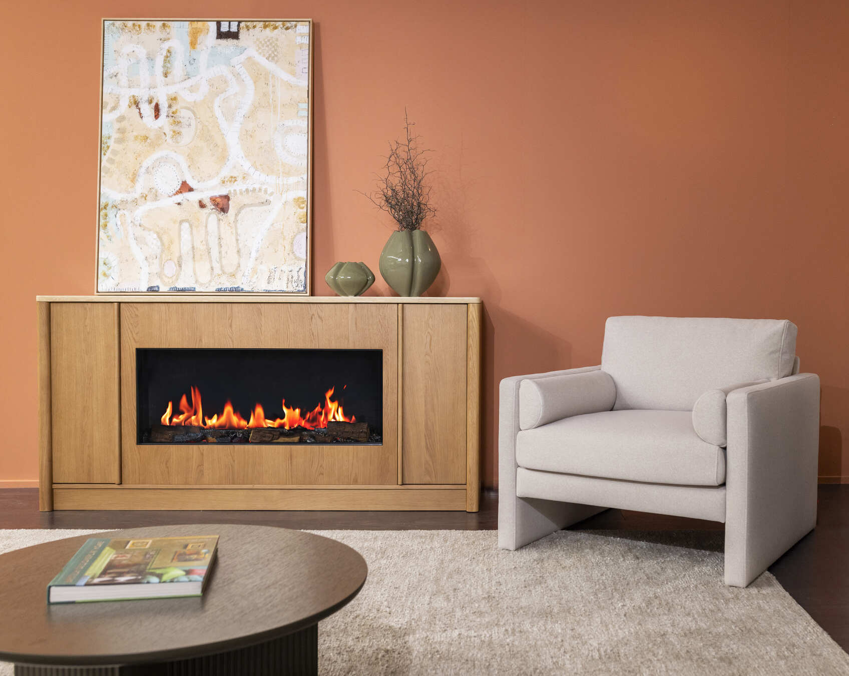 Ember Arc Grange 180 electric fireplace with wood-burning insert sits beneath a painting and vase beside a sofa chair in a modern living space