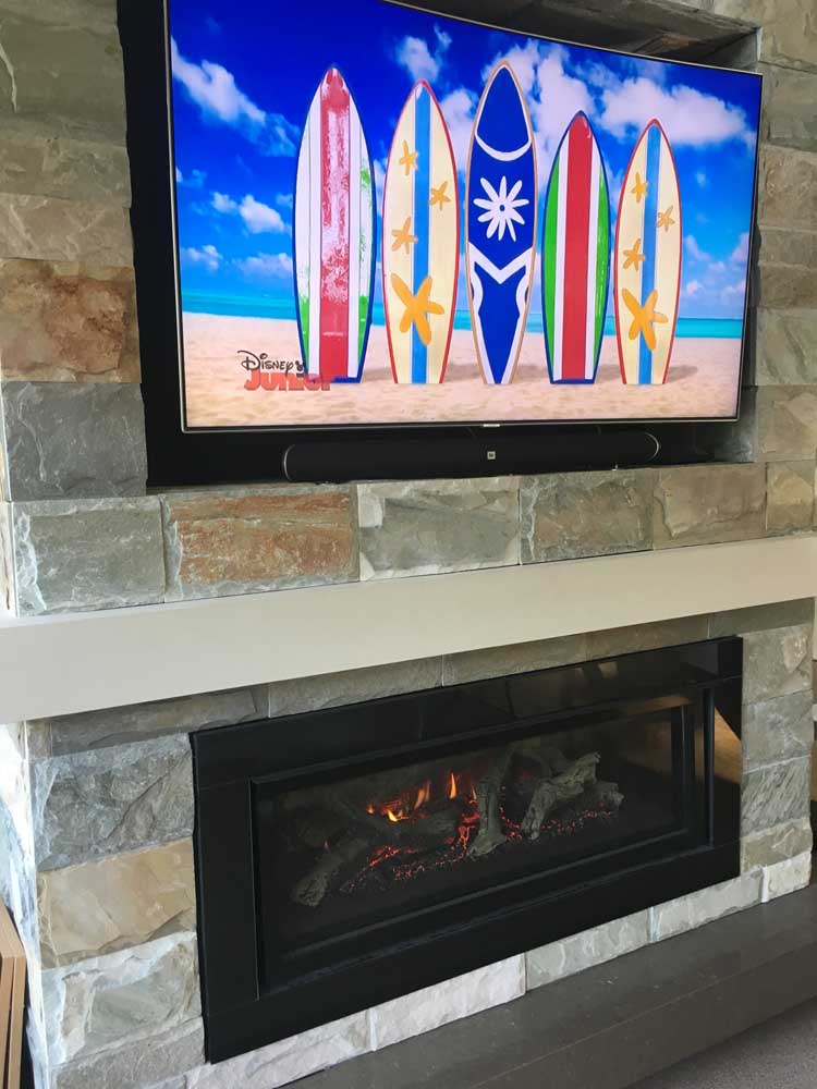 A TV mounted on a stone fireplace featuring a Regency Greenfire GF1500L Gas Fire, with surfboards displayed above it