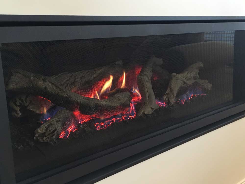 Close up of Regency Greenfire GF1500L gas fireplace with glowing flames and stacked logs, creating a warm ambiance