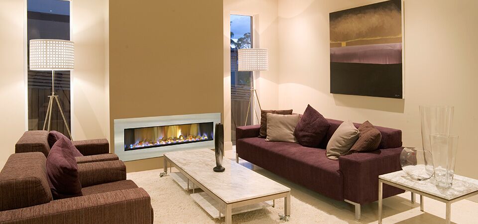 A plush couch with a painting above it and a Horizon Low Line Inbuilt Fireplace in a cosy living space, one of the best gas log heaters for autumn comfort and warmth