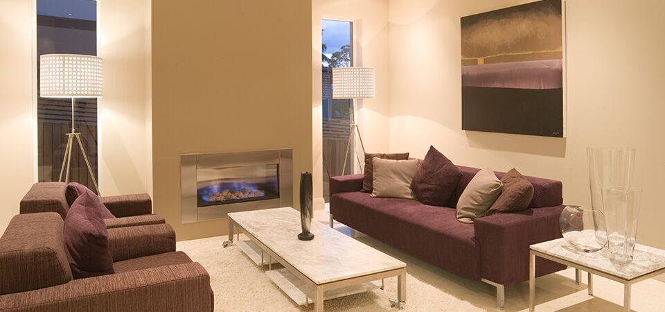 A plush couch with a painting above it and a Horizon Low Line Inbuilt Fireplace in a cosy living space, one of the best gas log heaters for autumn comfort and warmth