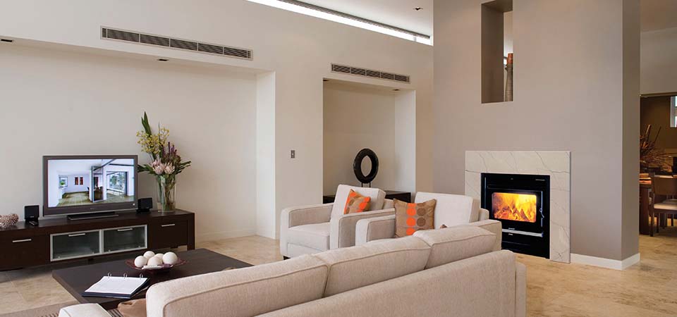 A cosy living room with a double-sided Kemlan Coupe fireplace beside a TV, one of the best wood heaters for autumn