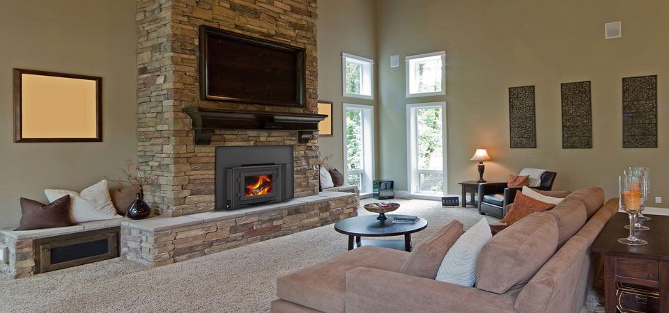 A cosy living room with a pink plush sofa and a Heatilator wood-burning insert topped with a TV, among the best wood heaters for autumn comfort