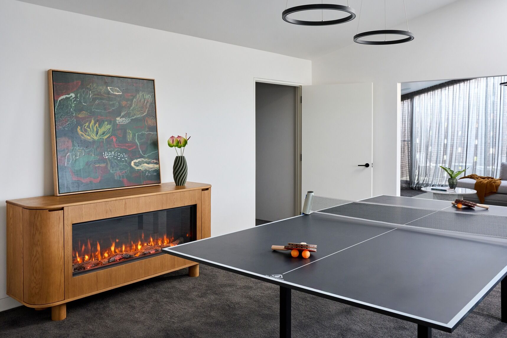 Ember Arc Grange 180 electric fireplace installed below a painting, with a wooden cabinet and table tennis setup nearby
