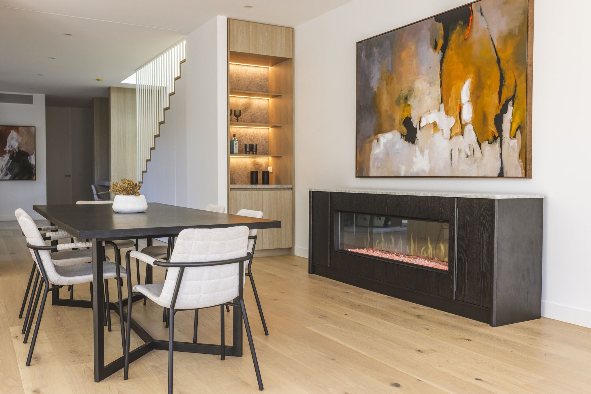 Modern dining room with an electric fireplace and artwork, with the Ember Arc Grange 240 integrated seamlessly into the interior design